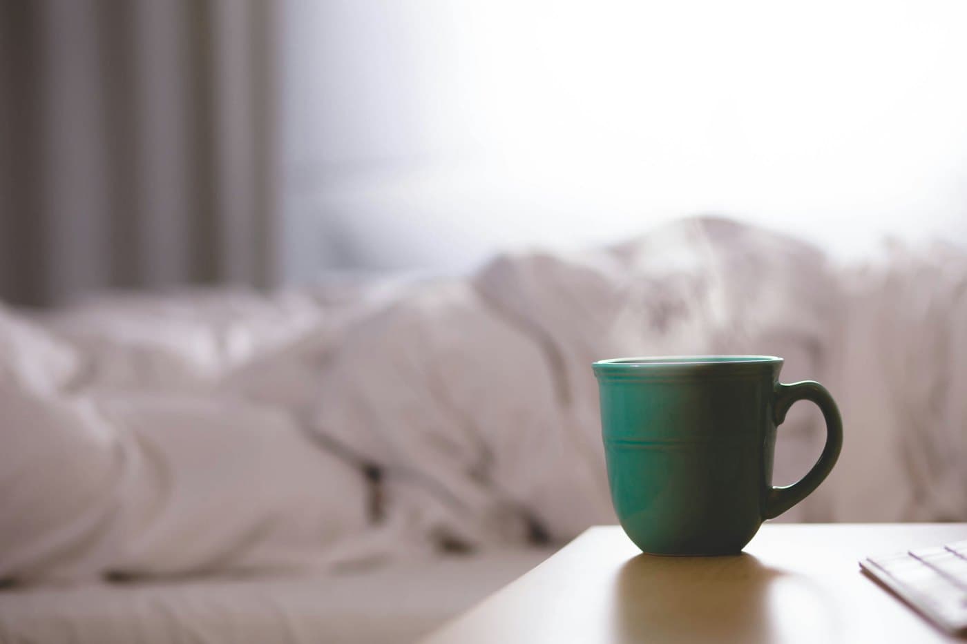 A quiet morning: a mug beside an unmade bed in soft light