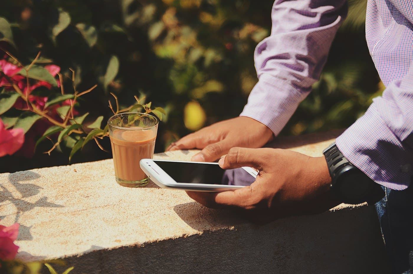 A person holding a phone in warm morning sun beside a cup of tea